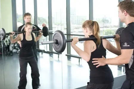 Übung im Fitnessstudio mit der Langhantel unter Anleitung eines Trainers